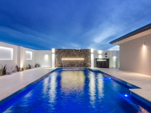 Compass X Trainer fibreglass pool with a water wall and lights on